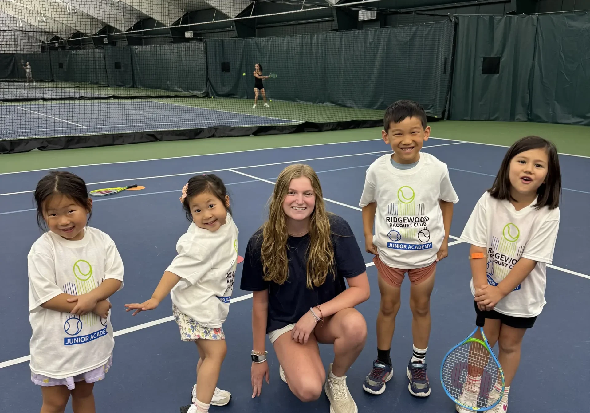 Group of children standing on top of a tennis court, each holding a tennis racket